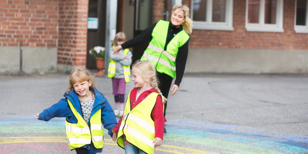 Pedagog och tre barn i gula reflexvästar leker på gård.