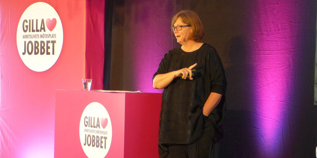 Lisbeth Rydén håller föredrag på Gilla jobbet. svart klänning, lila bakgrund.