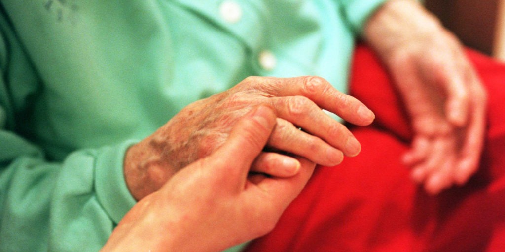 Närbild av händer, en yngre person håller i en äldre persons ena hand.