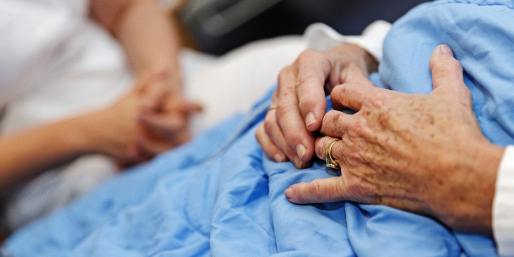 Närbild på en patients händer på ett blått täcke.