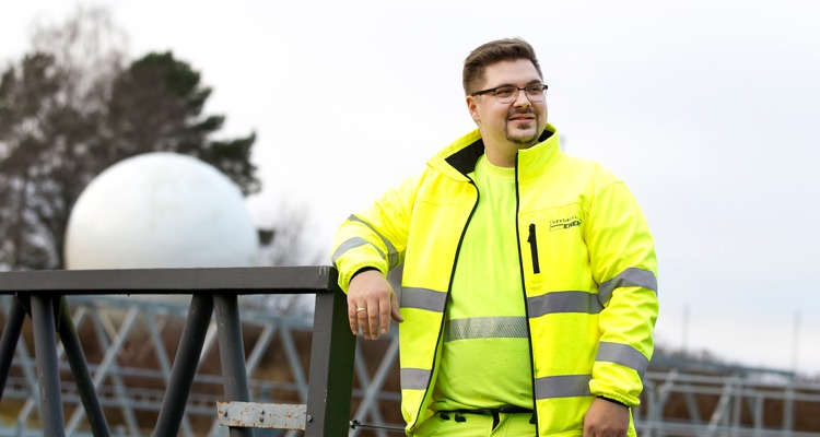 En man i gula varselkläder står utomhus och lutar armen mot ett staket.