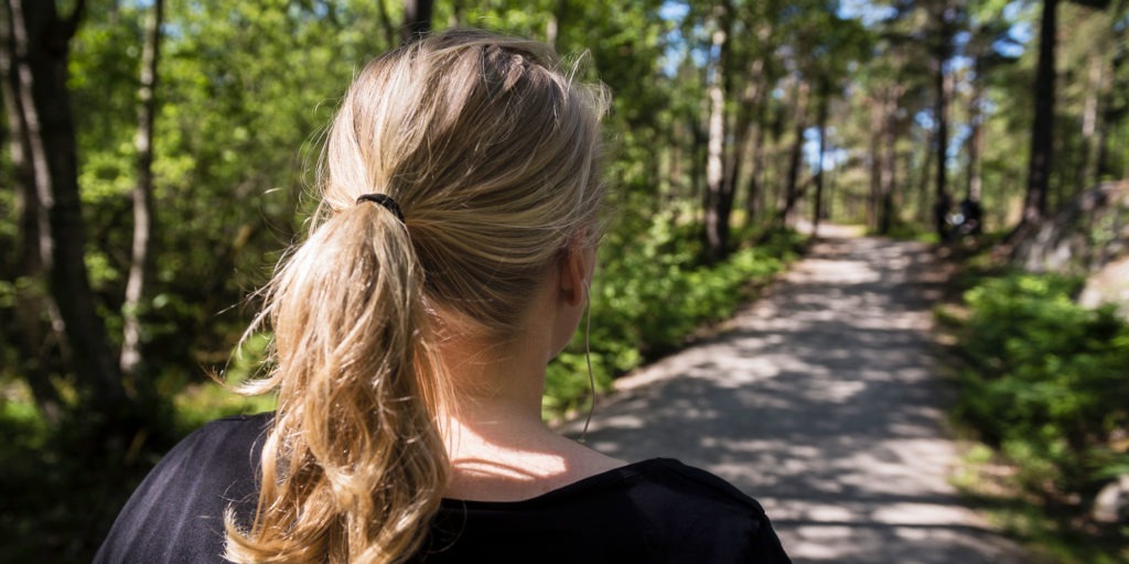 En kvinna är ute och promenerar på en skogsväg.