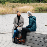 två kvinnor sitter och samtalar på en brygga, i höstväder