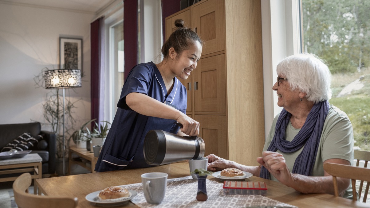 Kvinna som jobbar i hemtjänsten häller upp kaffe till brukare.