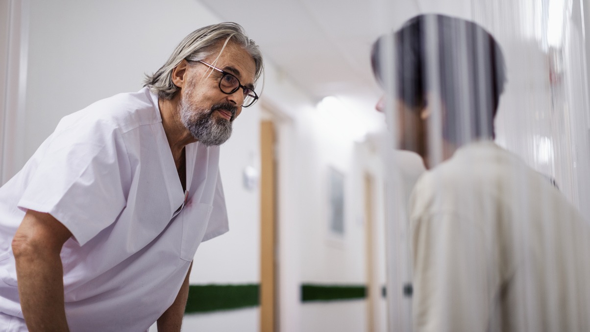 Sjukvårdare lutar sig fram emot en patient. Patienten sitter i en korridor.
