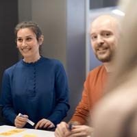 Fotoillustration till Forskning på 5: teamets betydelse. Två personer står vid ett bord och pratar med en tredje person utanför bilden.