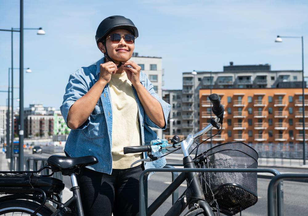 Kvinna som cykelpendlar till jobb sätter på sig cykelhjälm utanför kontorsbyggnader