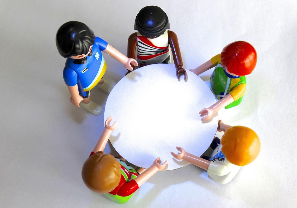 Fem leksaksgubbar Playmobil sedda uppifrån runt ett bord, tema effektiva möten.