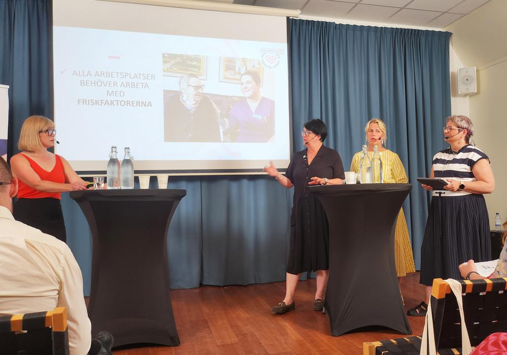 Fyra personer står och pratar på ett seminarium om friskfaktorer