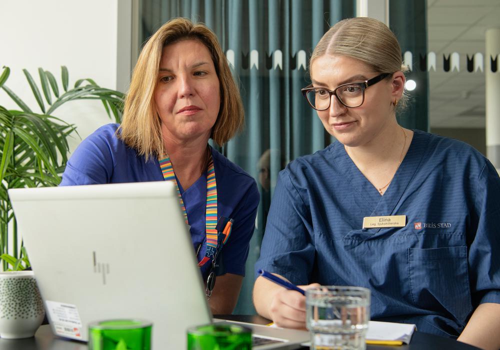 Sjuksköterskan Jessica Säll, mentor åt sjuksköterskan Elina Maksumic. De sitter tillsammans vid en dator och tittar engagerat på något på skärmen.