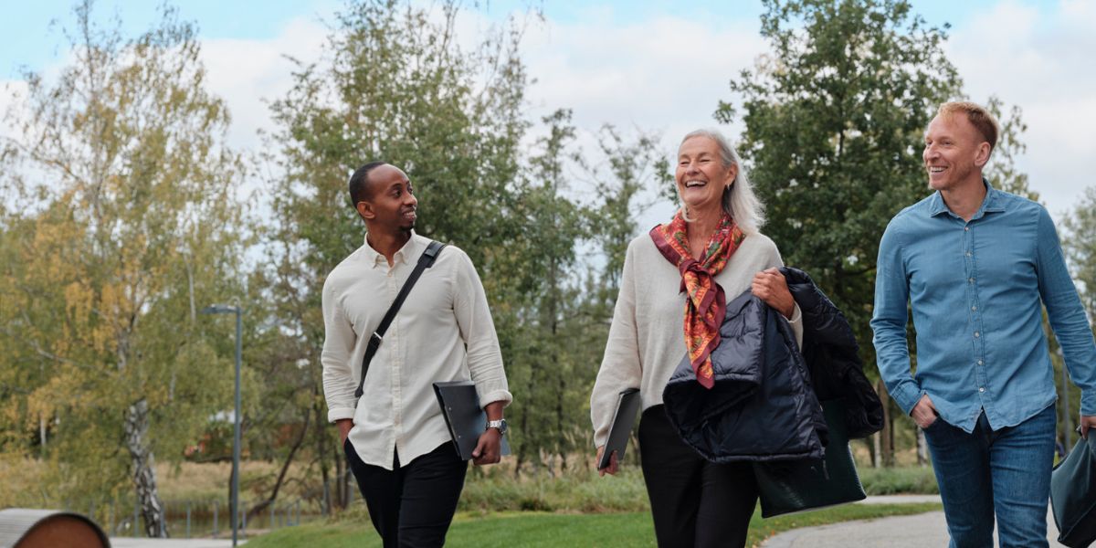 Tre kollegor promenerar utomhus och pratar med varandra.