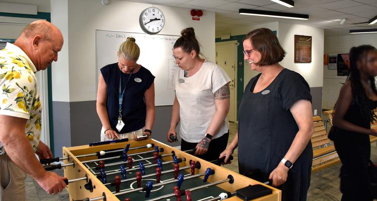 Skolpersonal spelar bordsfotbollsspel. Två är rektorer, två är lärare och arbetsmiljöombud.