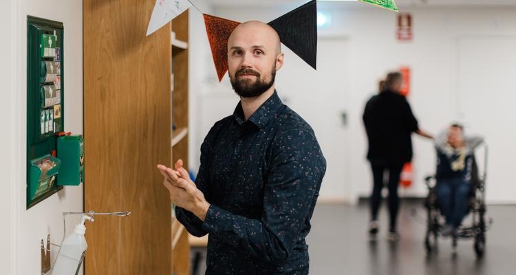 Enhetschefen Jonatan Dahlbo använder handsprit som finns lätt tillgänglig upphängd på väggen. I bakgrunden en person i rullstol.