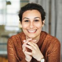 Leende kvinna med orange tröja tittar rakt fram.