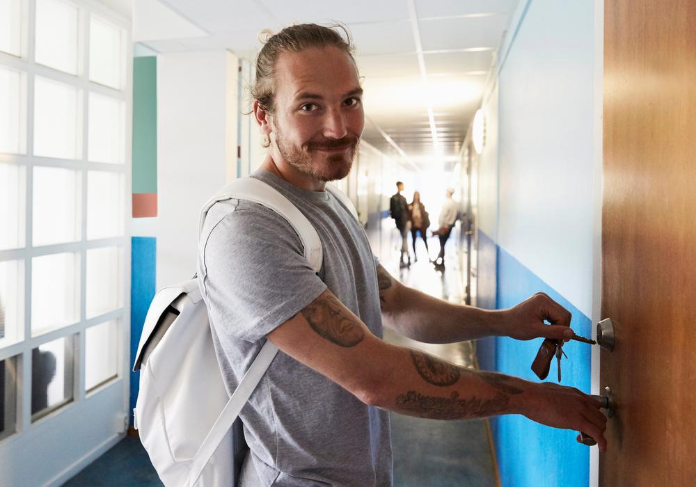 porträtt av en man som låser upp en dörr i en korridor, kanske i skolmiljö