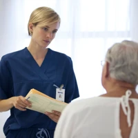 Vårdpersonal kvinna pratar med patient man som sitter och har ryggen mot kameran.