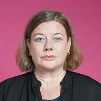 Malin Ragnegård, ordförande i Kommunal, talar om sexuella trakasserier på ett seminarium. Malin står i svart skjorta mot rosa bakgrund och ser allvarlig ut.