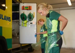 Två kvinnliga ambulansförare tar på förkläden utanför ambulansen.