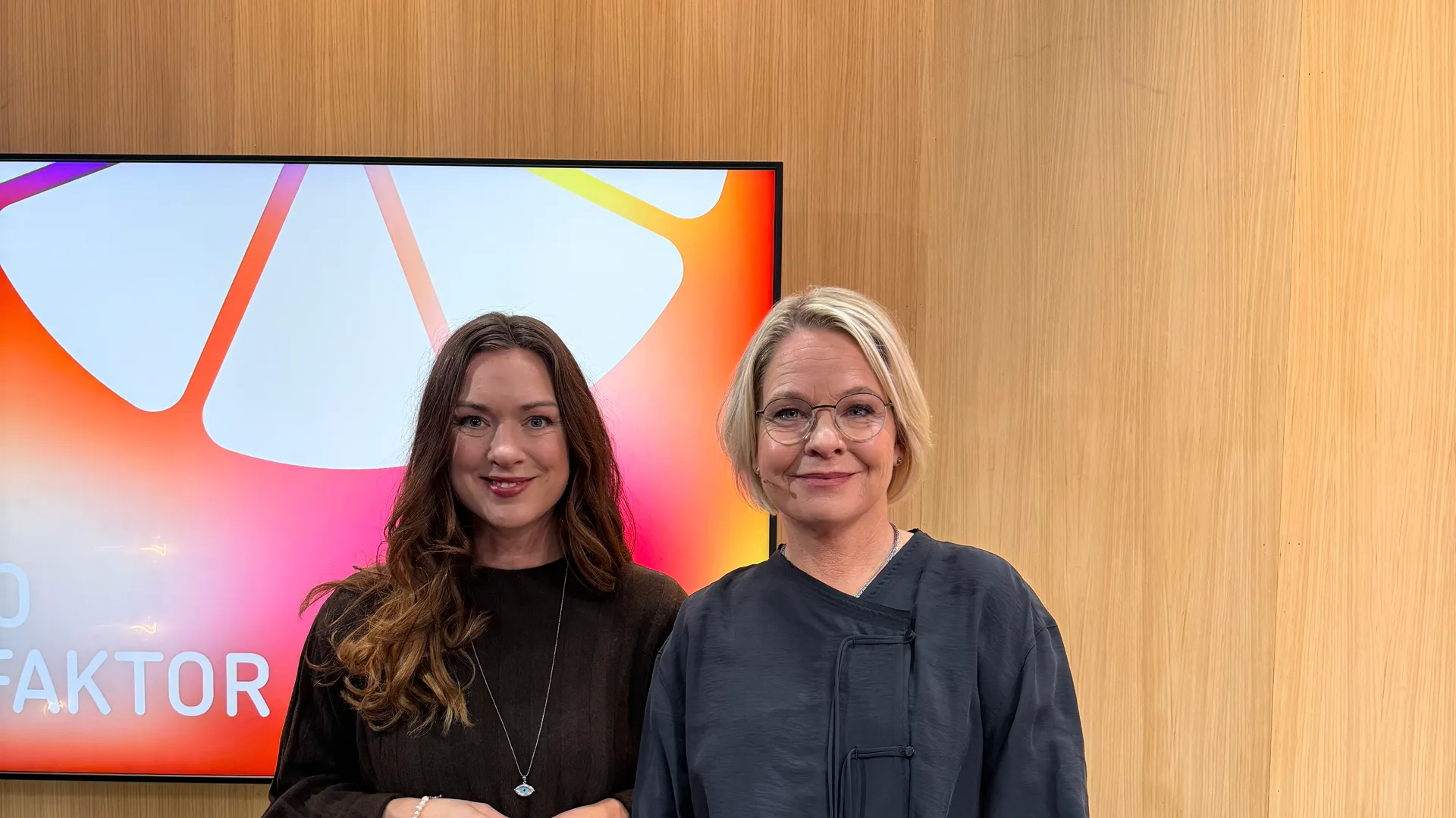 Två kvinnor står bredvid varandra framför en TV