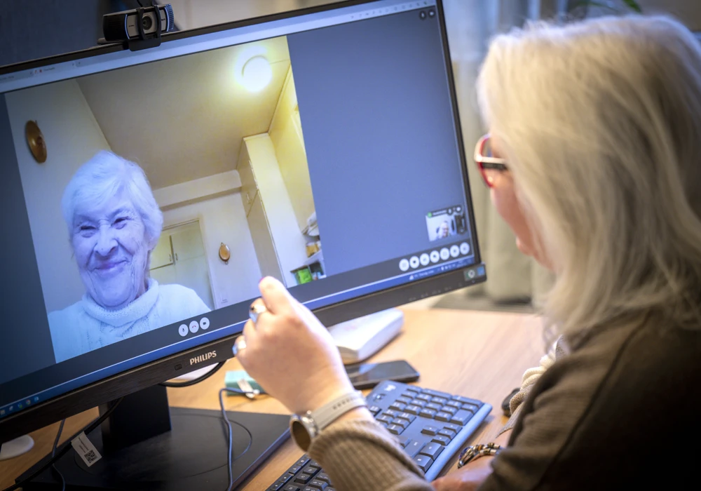 En kvinna sitter framför en datorskärm i videosamtal med äldre kvinna på skärmen.