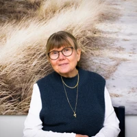 En kvinna med glasögon sitter framför en målning
