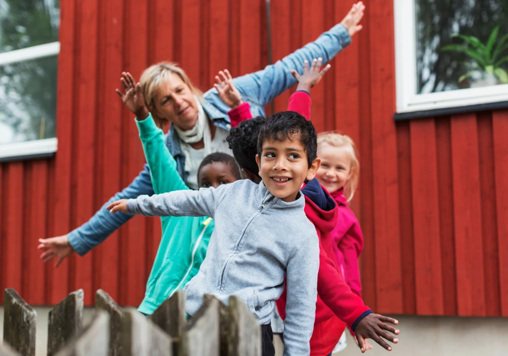 En grupp förskolebarn utomhus som leker flygplan tillsammans med pedagog, tema ljudkänslighet.