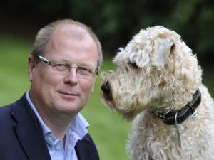 Porträttbild av medelålders man tillsammans med en vit hund.