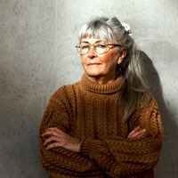 äldre kvinna i tjock brun tröja tittar in i kameran.