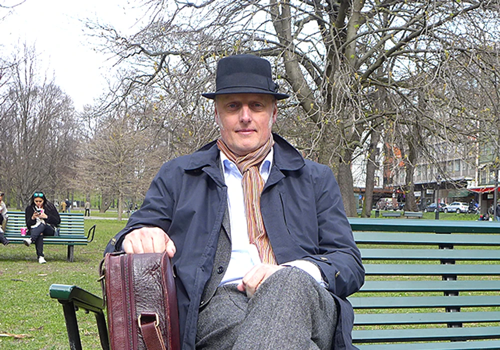 Hejlskov sitter på en parkbänk med portfölj och hatt.