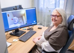 en kvinna vid en dator. På skärmen syns en brukare som får digital hemtjänst i Lund.
