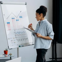 En kvinna står framför en whiteboardtavla med diagram och tabeller.