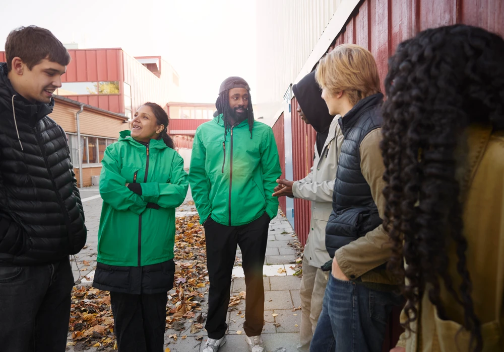 Två fältarbetare står utomhus och pratar med en grupp ungdomar.