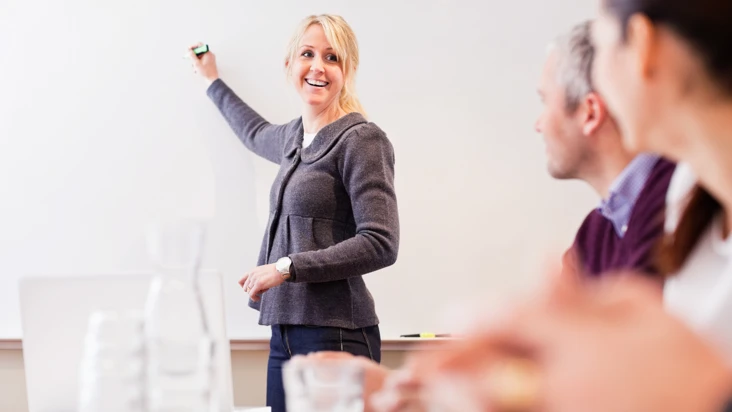 Kvinna förklarar och skriver på en whiteboard för kollegor.