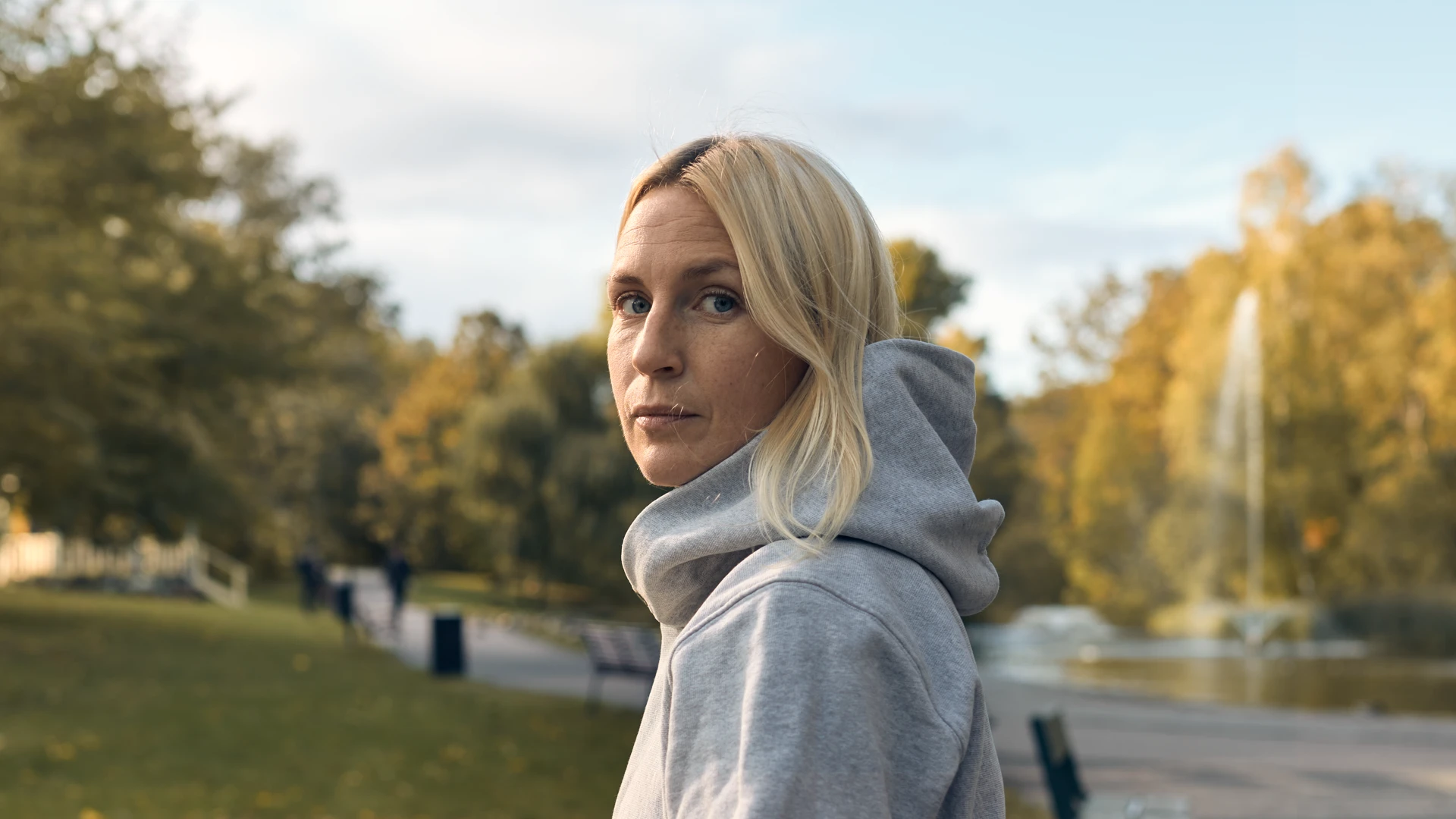 Ljushårig kvinna med grå luvtröja tittar rakt in i kameran.
