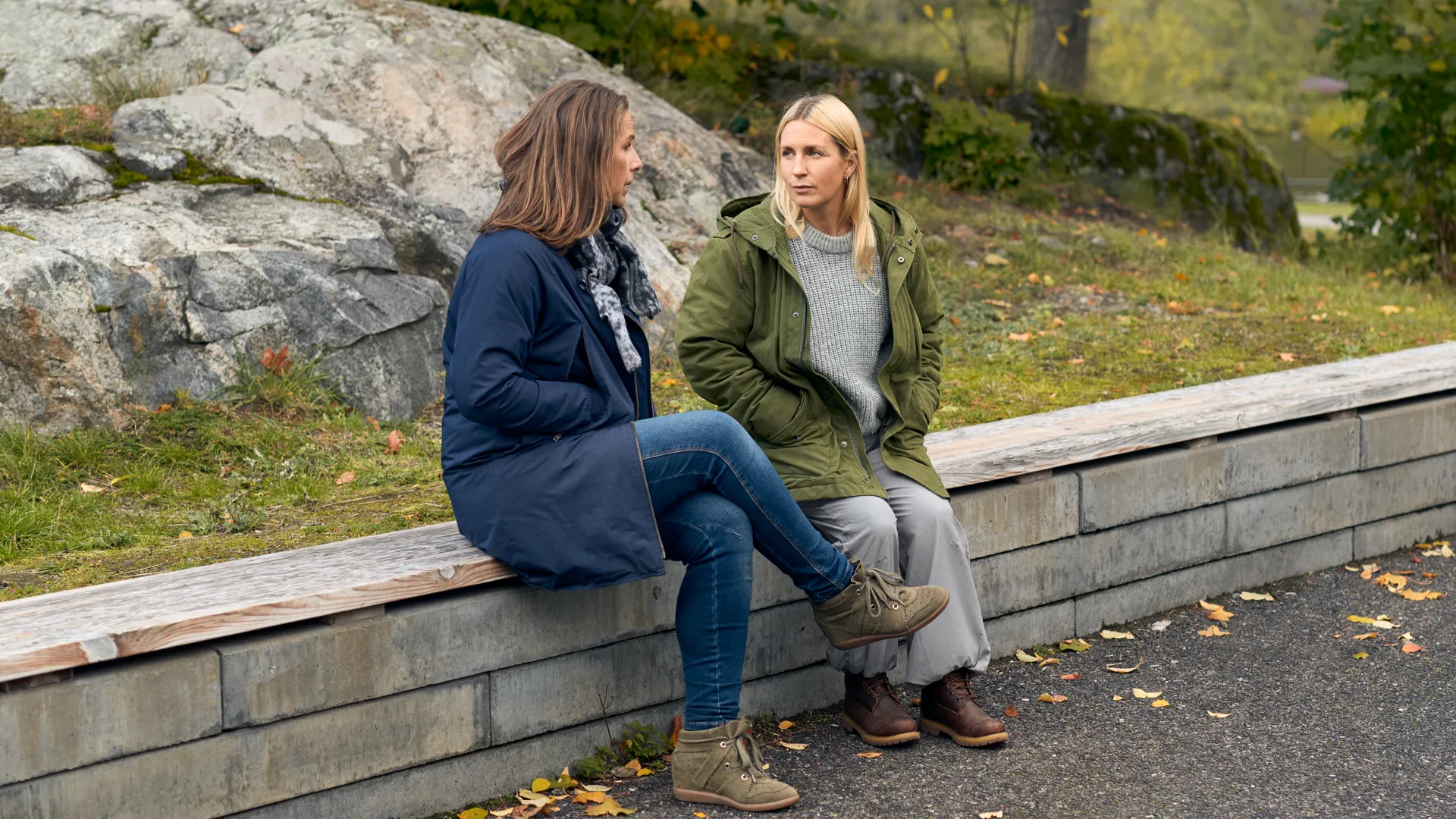 Två kvinnor sitter på en mur utomhus och pratar.