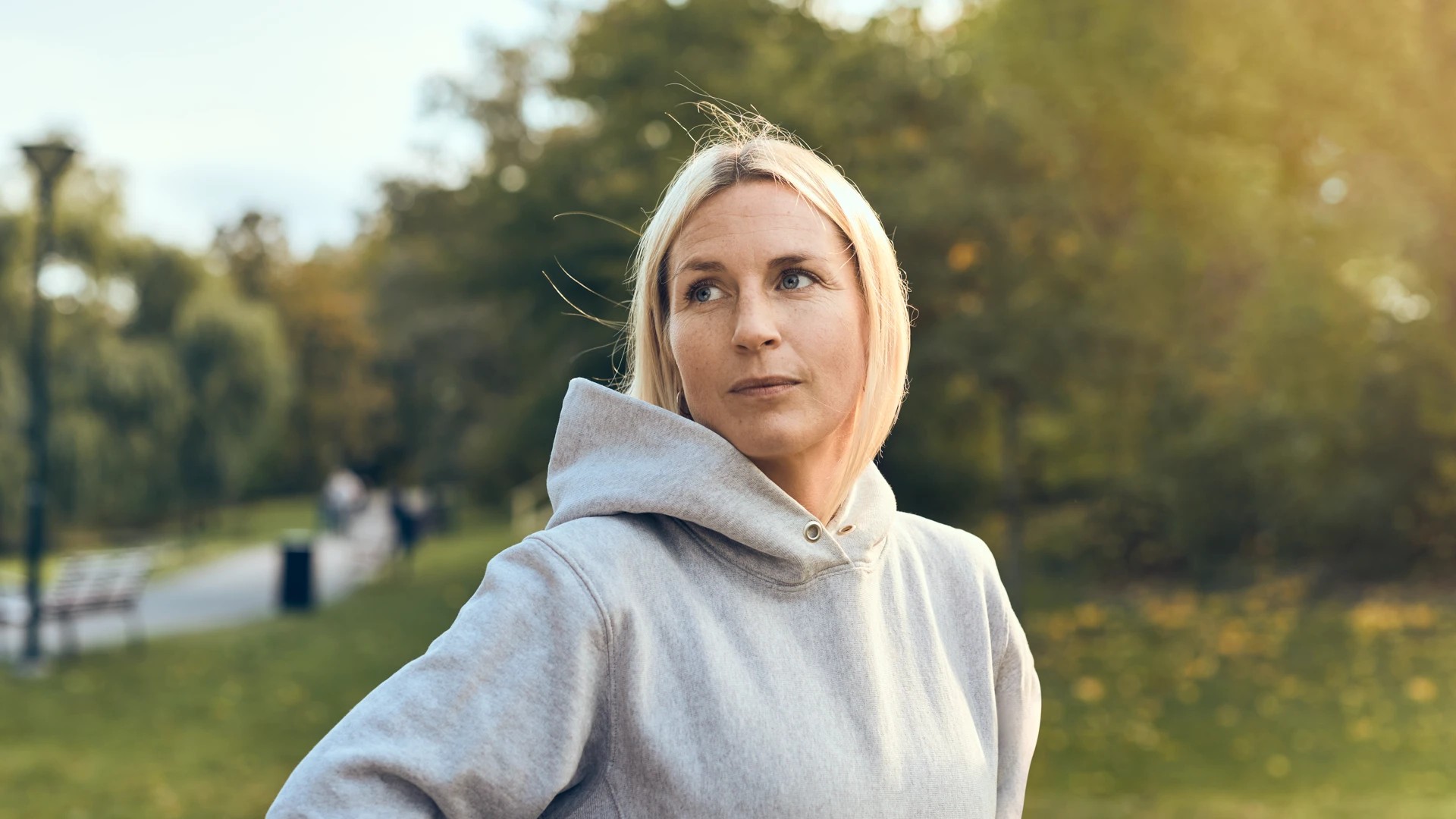 Kvinna i grå huvtröja står på en gräsmatta.