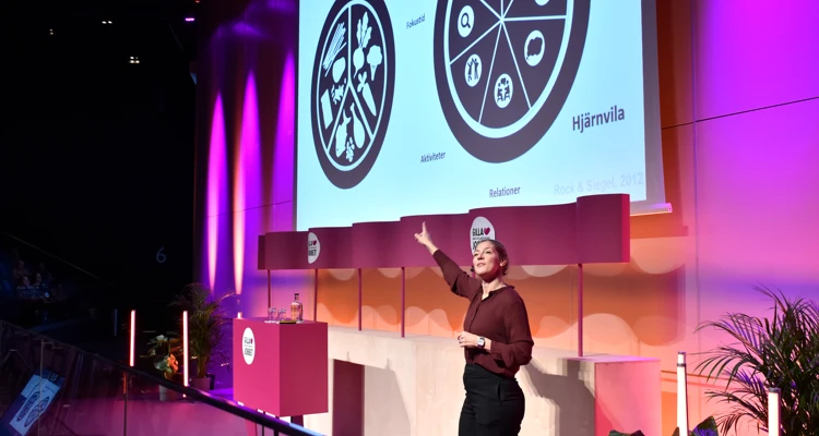 Kvinna på scen håller presentation och pekar på tallriksmodell där hjärnvila ingår.