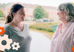 Två kvinnor som samtalar utomhus och ler mot varandra.