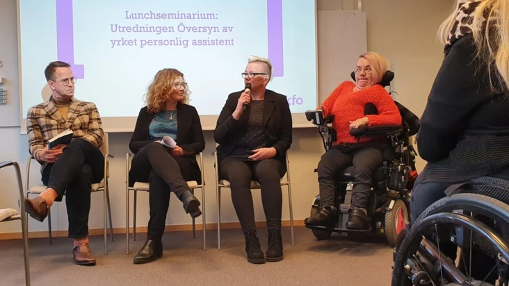 En grupp människor som sitter i stolar och rullstolar framför en projektorduk.