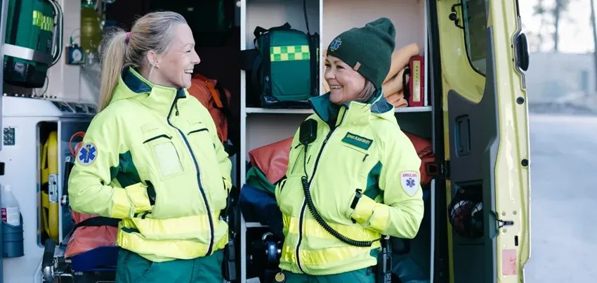Två kvinnor i ambulanskläder står och pratar.