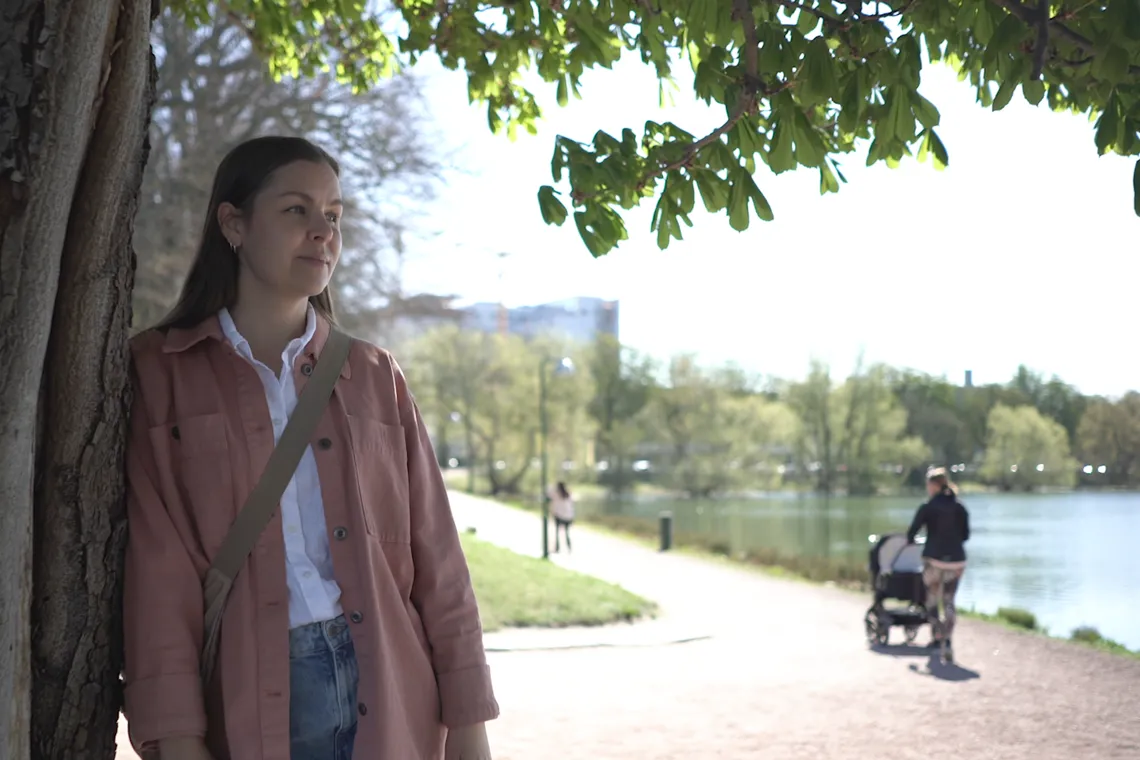 En kvinna som står bredvid ett träd i en park.
