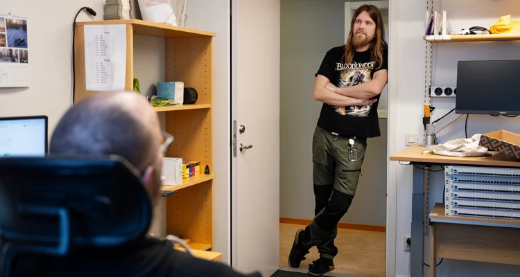 Man på kontor står och pratar med kollega som sitter.
