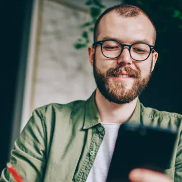 En man sitter vid ett bord och tittar på en mobiltelefon.