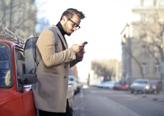 En man står bredvid en bil och tittar på sin mobiltelefon.