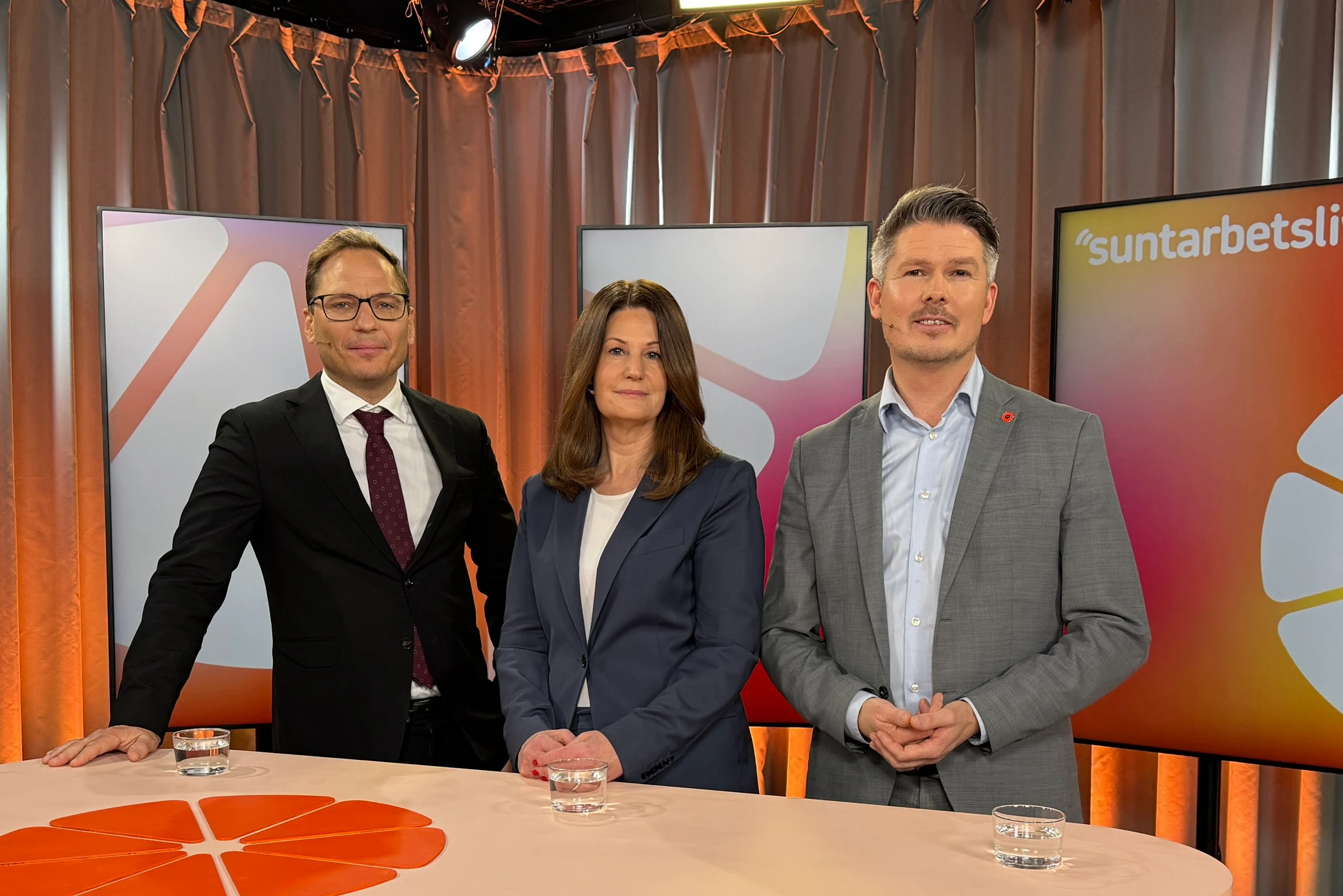 Tre personer som representerar parterna står vid ett bord i en studio.