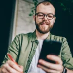 En man sitter vid ett bord och tittar på en mobiltelefon.